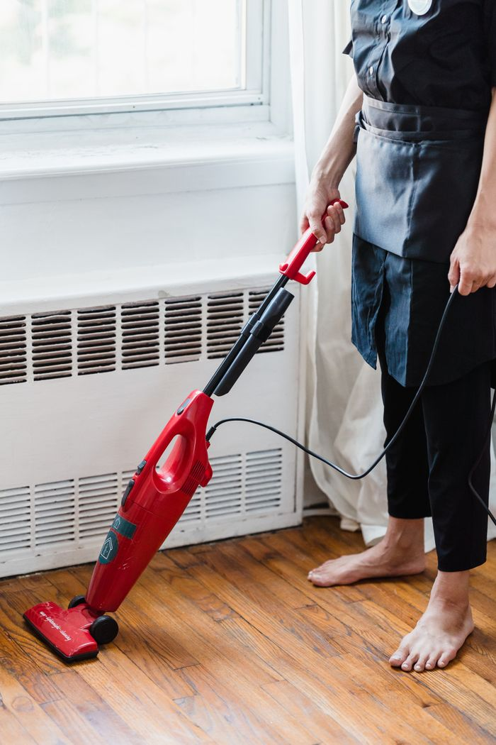 Person cleaning wooden floor with red vacuum cleaner in a well-lit room.